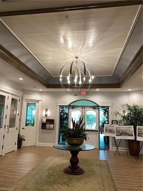 Entryway with crown molding, a tray ceiling, a chandelier, wood finished floors, and baseboards