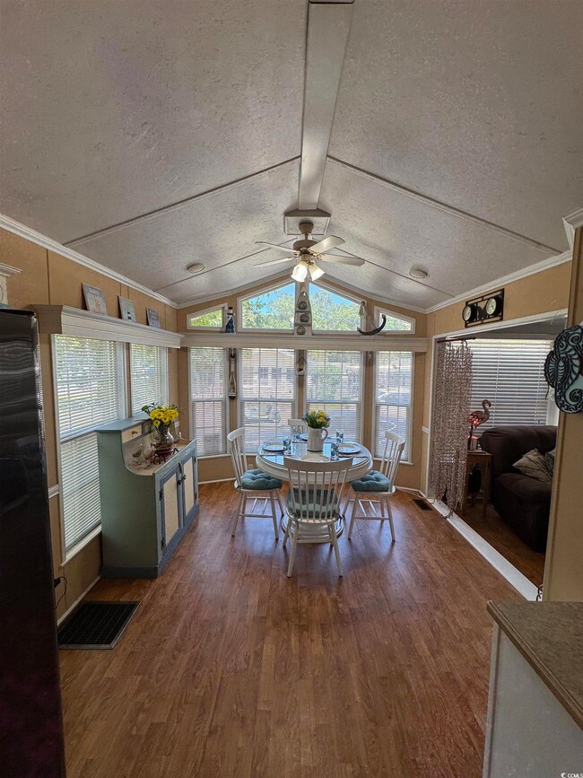 Dining space with a ceiling fan, a textured ceiling, wood finished floors, vaulted ceiling, and crown molding