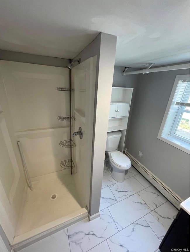 Bathroom with a baseboard heating unit, a shower stall, light marble finish floors, and vanity