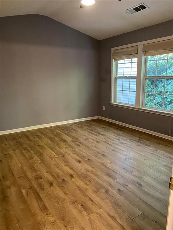 Empty room with wood finished floors and vaulted ceiling