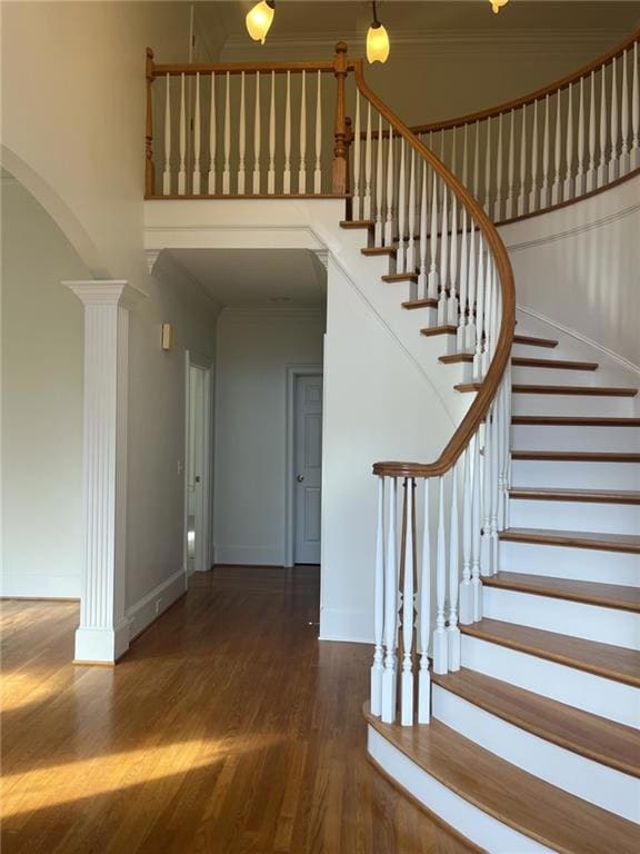 Stairs featuring ornamental molding, wood finished floors, arched walkways, and decorative columns