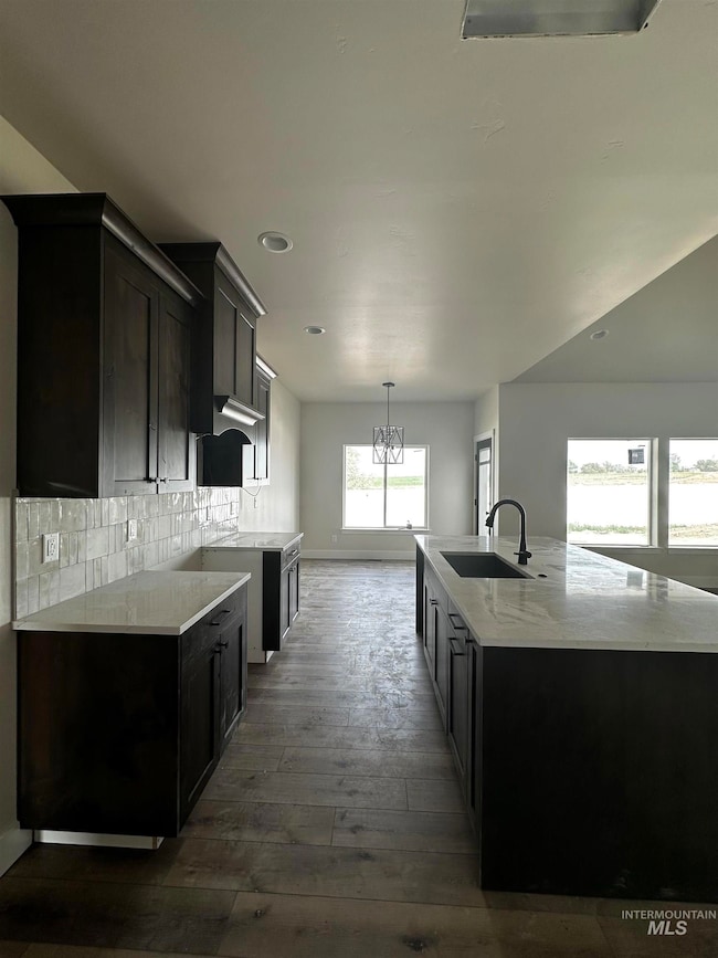 Kitchen with dark wood-style floors, backsplash, recessed lighting, a chandelier, and light stone countertops