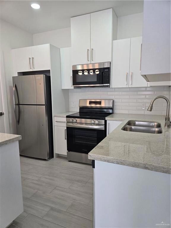 Kitchen featuring white cabinets, stainless steel electric range, a sink, decorative backsplash, and refrigerator