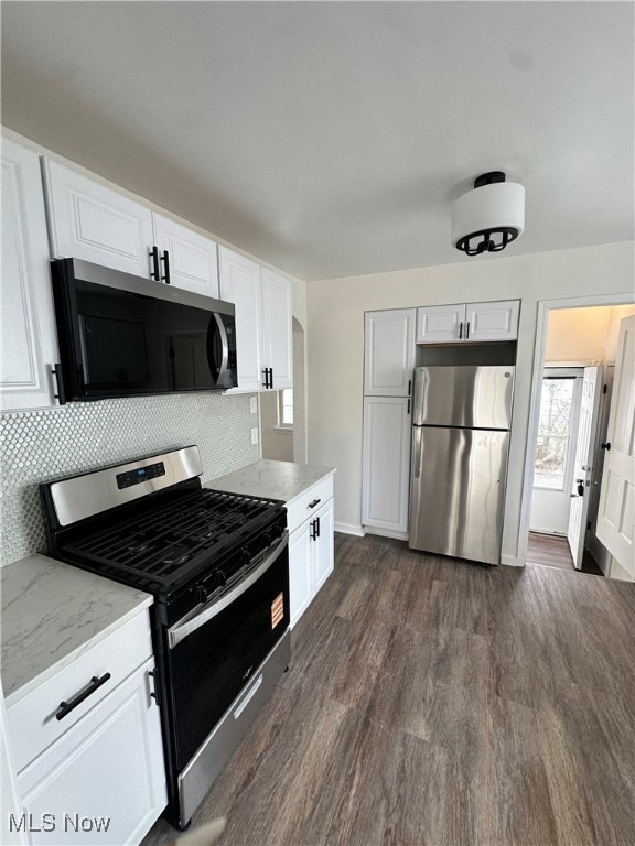 Kitchen featuring stainless steel appliances, white cabinets, dark wood-style floors, backsplash, and light stone counters