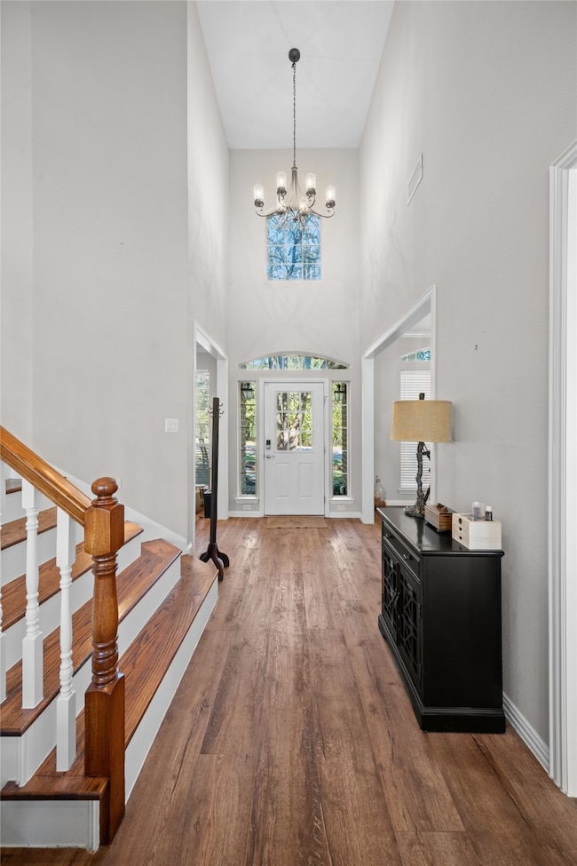 Entrance foyer featuring dark wood-type flooring, a towering ceiling, a chandelier, and stairs