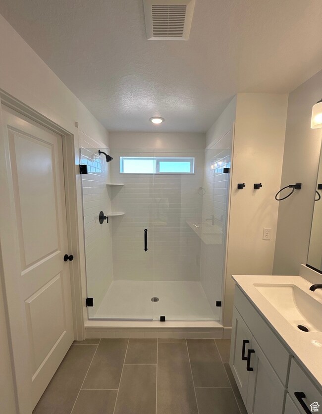 Full bath with vanity, a shower stall, dark tile patterned flooring, and a textured ceiling