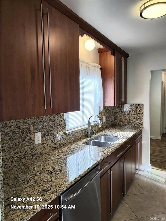 Kitchen with light stone countertops, backsplash, dark brown cabinets, stainless steel dishwasher, and light tile patterned floors