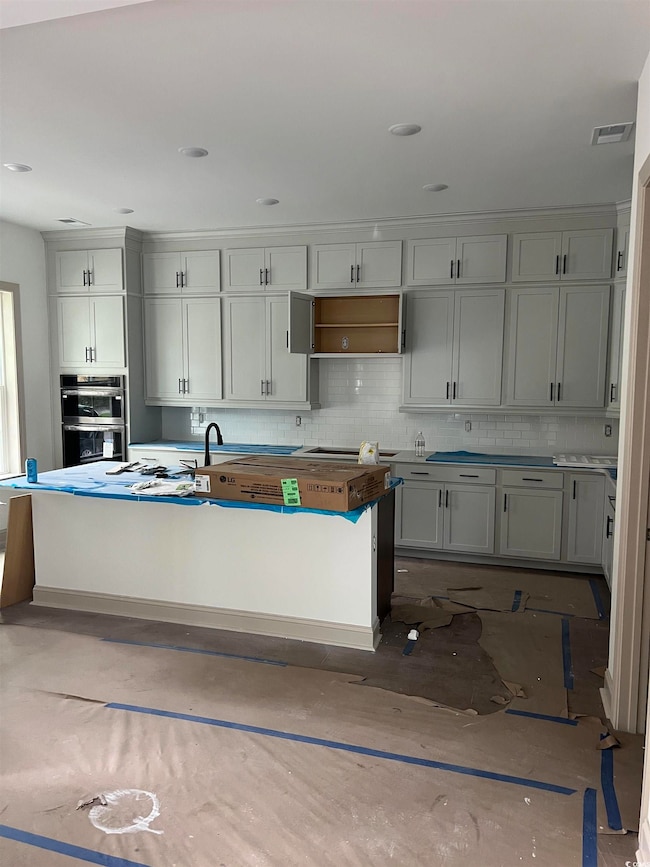 Kitchen with decorative backsplash, a center island with sink, stainless steel double oven, recessed lighting, and white cabinets