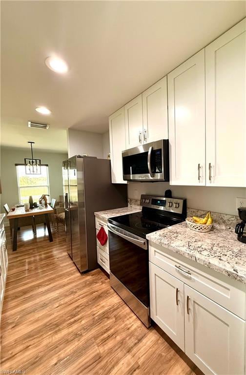 Kitchen featuring appliances with stainless steel finishes, white cabinets, light wood finished floors, light stone counters, and recessed lighting