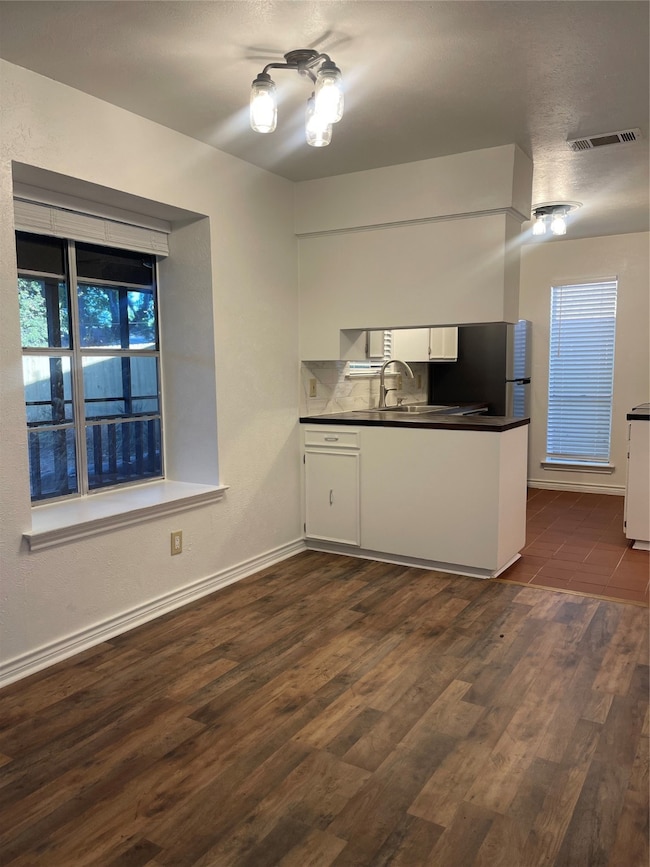 Kitchen with white cabinets, dark wood-type flooring, dark countertops, and fridge