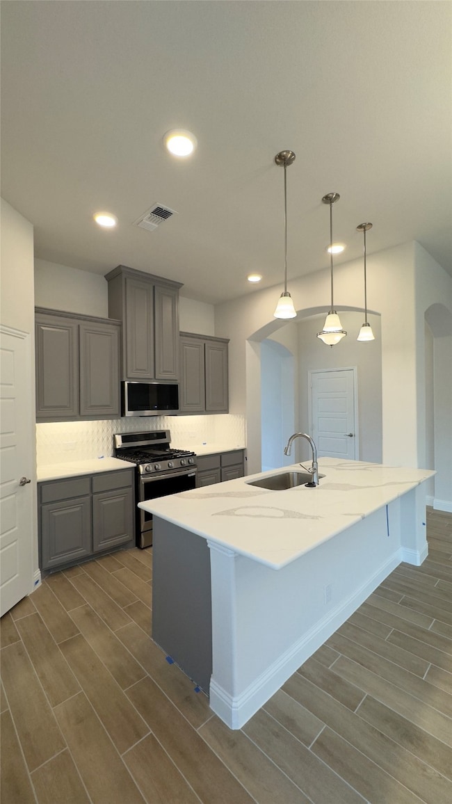 Kitchen with stainless steel appliances, gray cabinetry, wood finish floors, backsplash, and recessed lighting