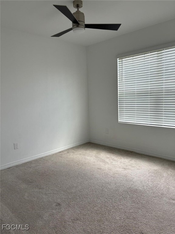 Carpeted empty room featuring baseboards and a ceiling fan