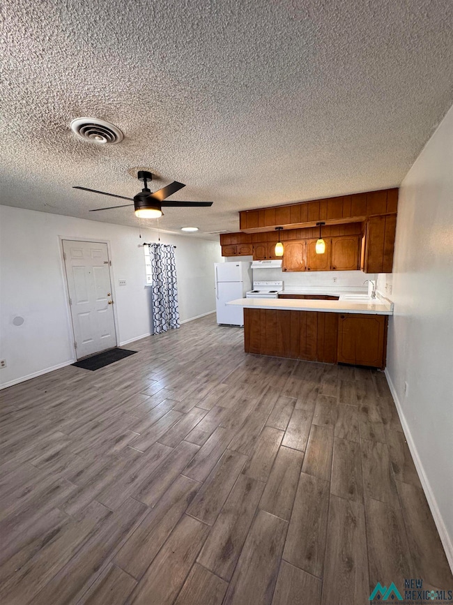 Kitchen featuring brown cabinetry, light countertops, open floor plan, dark wood-type flooring, and a textured ceiling