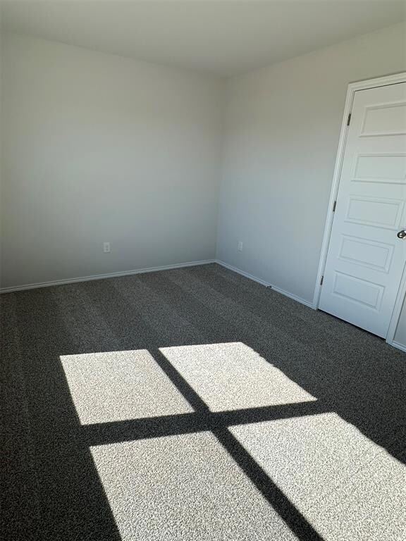 Empty room featuring dark colored carpet and baseb