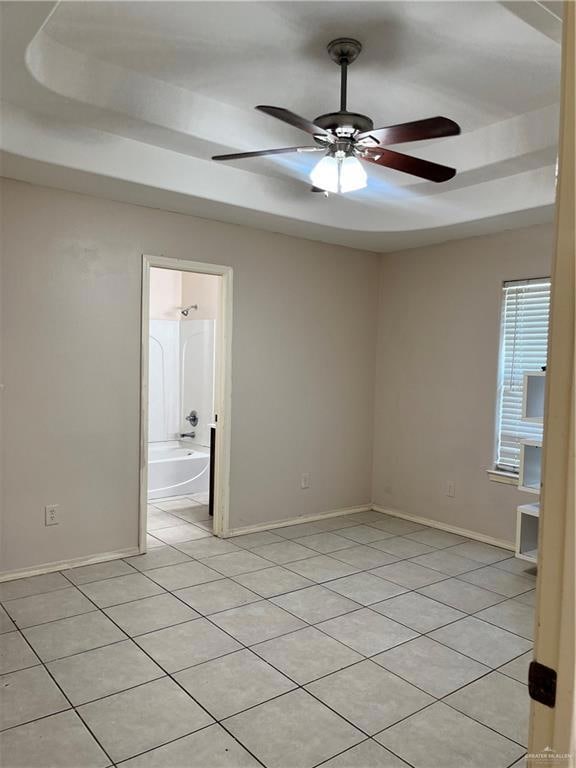 Tiled spare room featuring ceiling fan and a tray ceiling