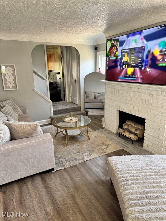 Living area featuring wood finished floors, a textured ceiling, arched walkways, a brick fireplace, and stairway
