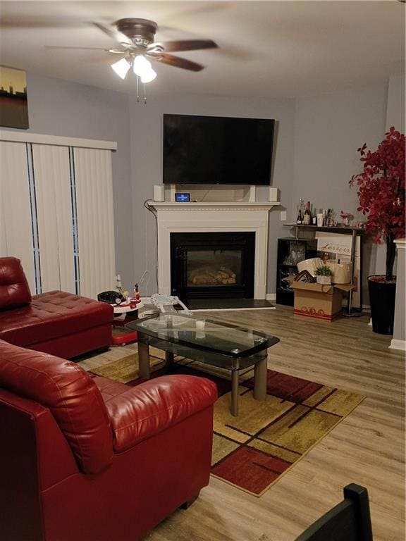 Living area featuring a glass covered fireplace, wood finished floors, and a ceiling fan