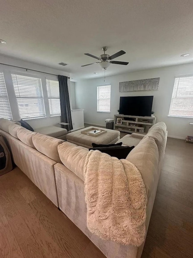 Living room with a ceiling fan, visible vents, pl