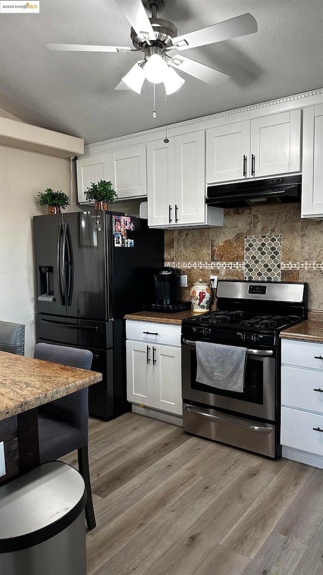 Kitchen with gas range, black refrigerator with ice dispenser, ceiling fan, extractor fan, and light wood-style flooring