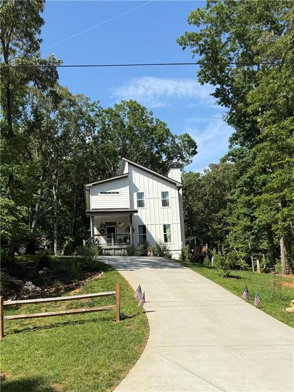 View of front facade featuring driveway, a front yard, board and batten siding, and a chimney