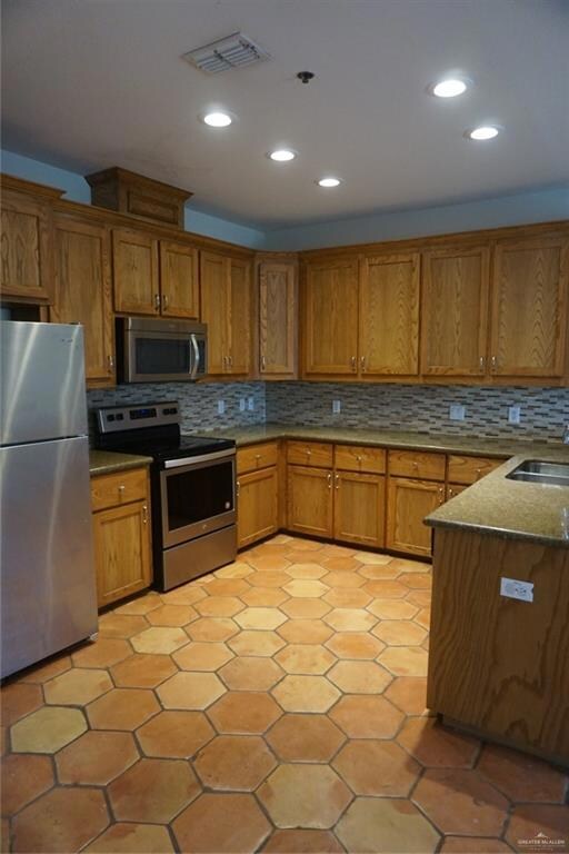 Kitchen with light tile floors, range, backsplash, refrigerator, and dark stone countertops