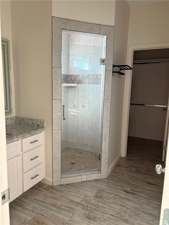 Full bathroom with light wood finished floors, a walk in closet, a shower stall, and vanity