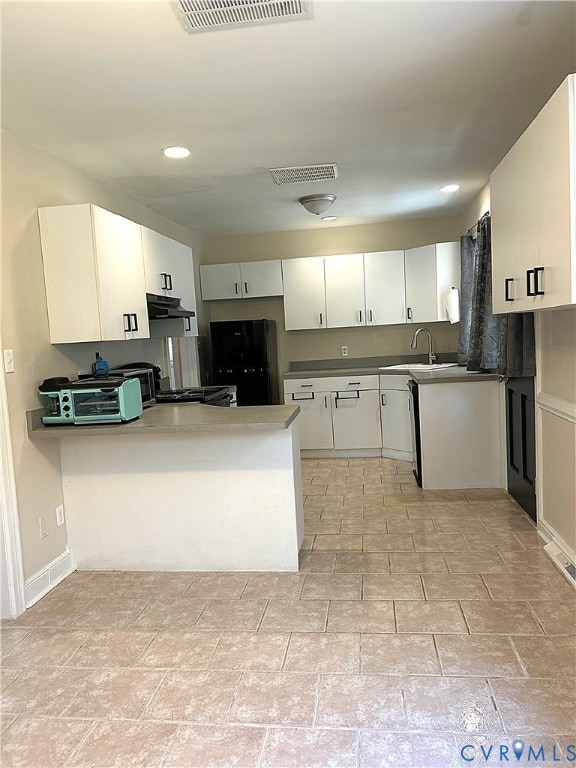 Kitchen featuring white cabinetry, a peninsula, freestanding refrigerator, recessed lighting, and light stone finish flooring