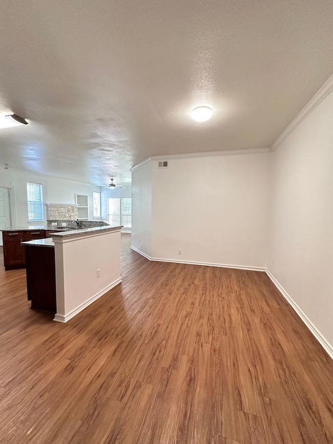 Unfurnished living room featuring light wood-style floors, a textured ceiling, crown molding, and ceiling fan
