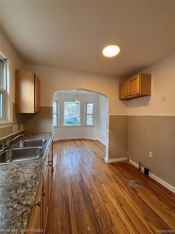 Kitchen with arched walkways, brown cabinets, dark wood-type flooring, and hanging light fixtures
