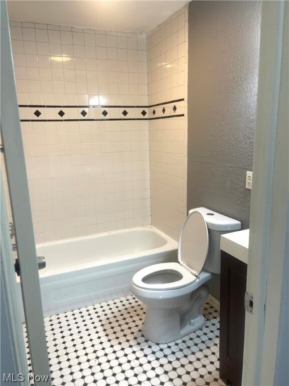 Full bathroom with tiled shower / bath combo, tile floors, vanity, and toilet