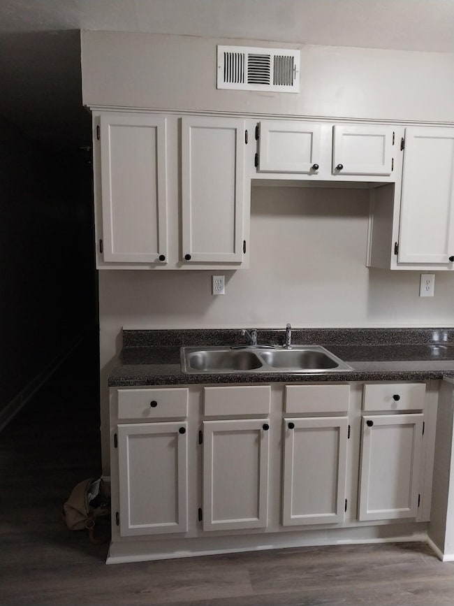 Kitchen with dark countertops, wood finished floors, and white cabinetry