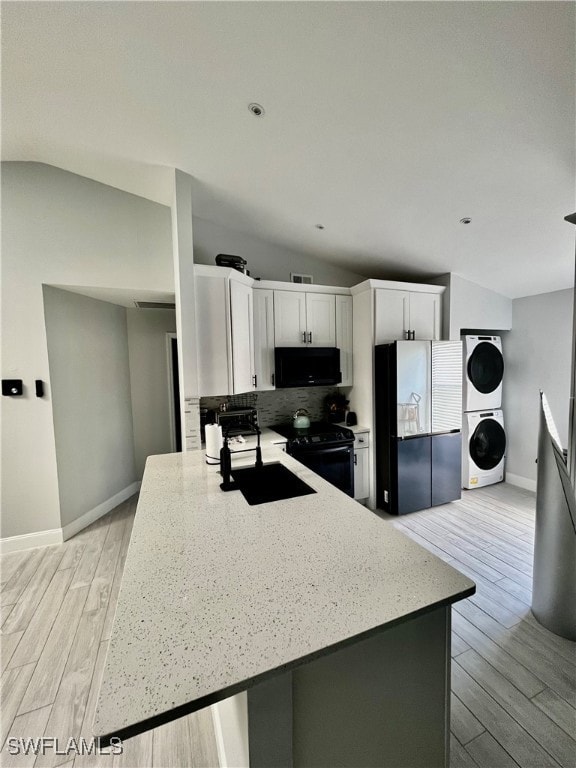 Kitchen with stacked washing machine and dryer, light Spanish tile flooring, electric range, decorative backsplash, and white cabinetry