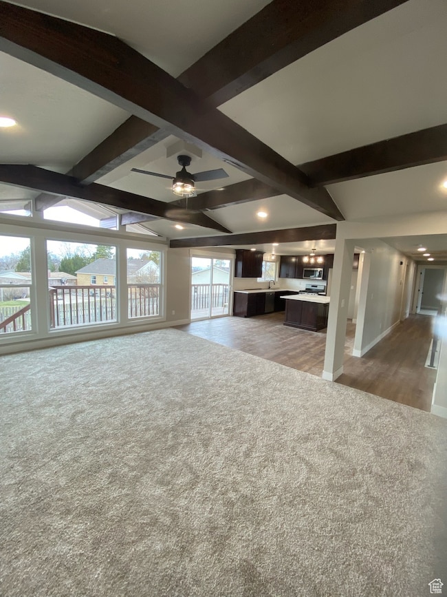 Unfurnished living room featuring vaulted ceiling with beams, light colored carpet, baseboards, and ceiling fan