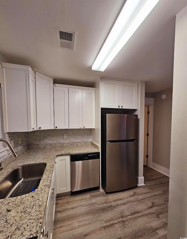 Kitchen with white cabinetry, appliances with stainless steel finishes, light wood-style flooring, light stone counters, and tasteful backsplash