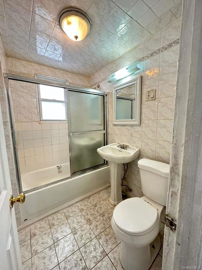 Bathroom with tile walls, light tile patterned floors, and bath / shower combo with glass door