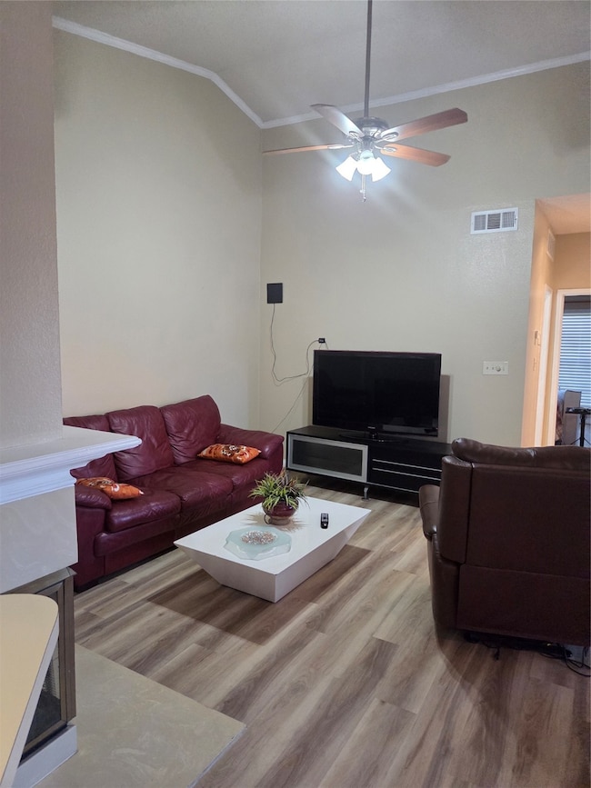 Living room with wood finished floors, crown molding, ceiling fan, visible vents, and lofted ceiling