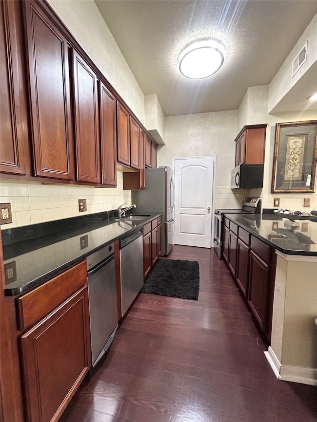 Kitchen with dark wood-type flooring, stainless steel appliances, tasteful backsplash, and dark stone countertops