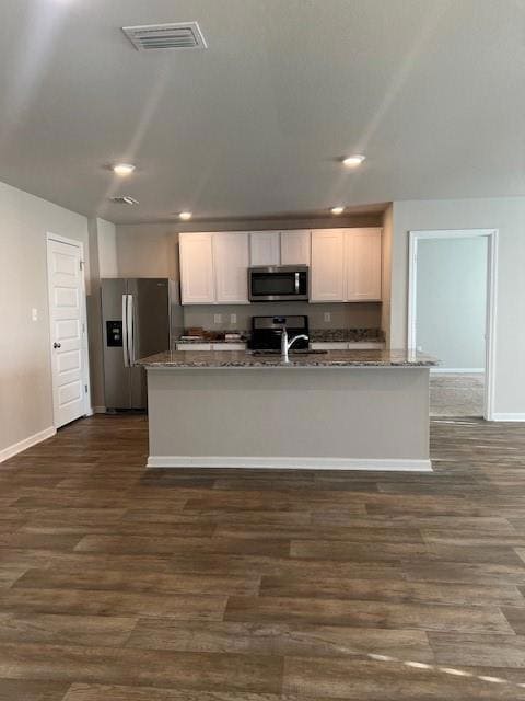 Kitchen with stainless steel appliances, white cabinets, dark wood-type flooring, dark stone counters, and recessed lighting