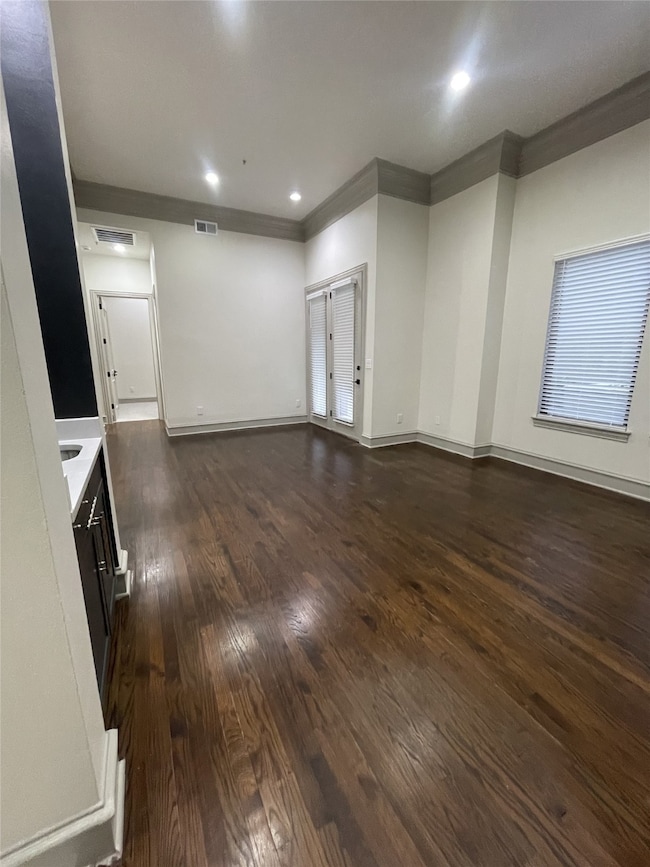 Unfurnished living room with dark wood-type flooring, crown molding, and recessed lighting