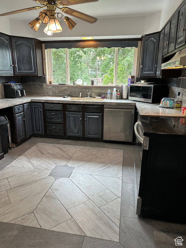 Kitchen with decorative backsplash, dark cabinetry, stainless steel appliances, and a ceiling fan
