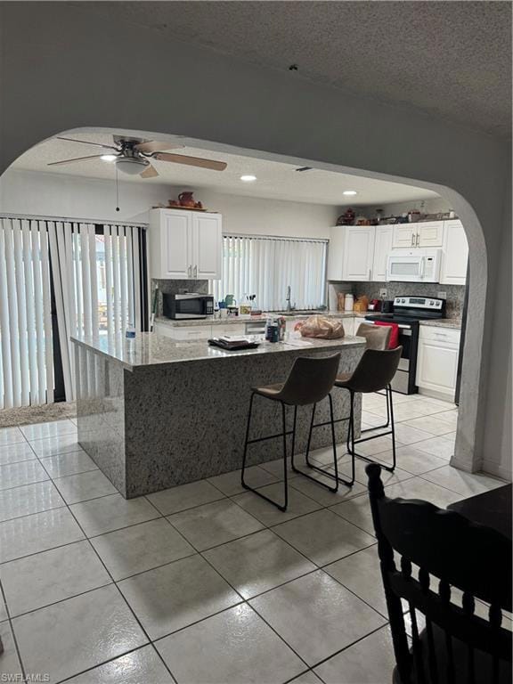 Kitchen with arched walkways, ceiling fan, stove, and tasteful backsplash