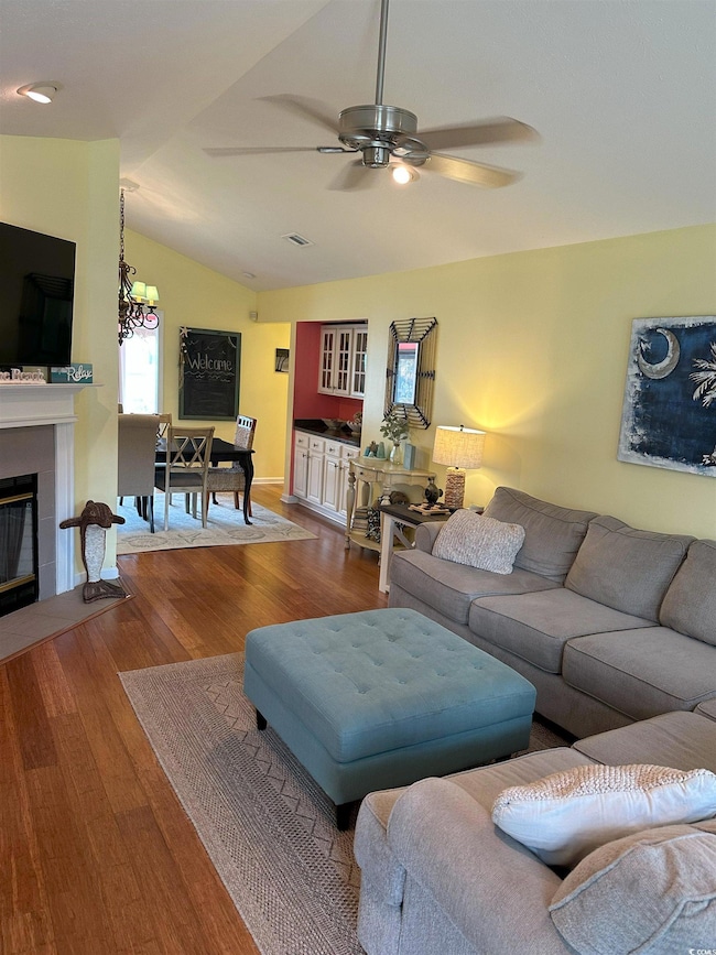 Living area featuring ceiling fan, a tile fireplace, wood finished floors, and vaulted ceiling