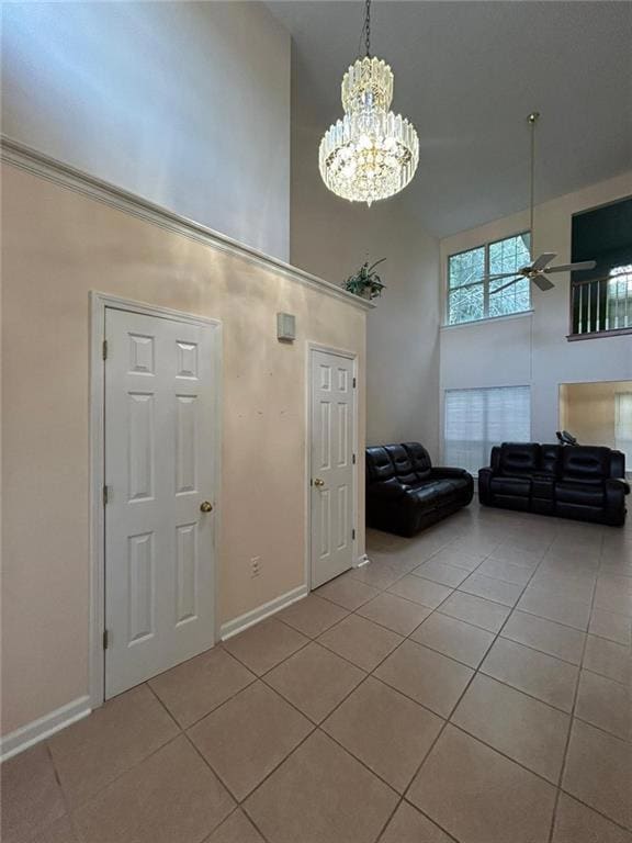 Foyer entrance with a high ceiling, light tile patterned flooring, ceiling fan, and a chandelier