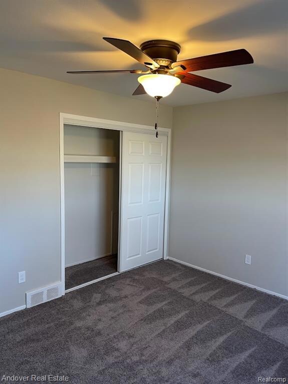 Unfurnished bedroom with dark colored carpet, a closet, and ceiling fan
