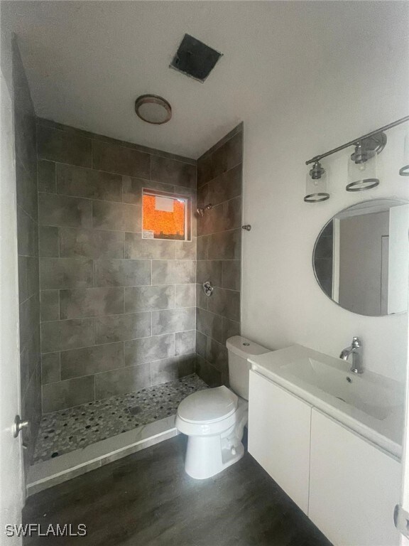 Bathroom featuring toilet, tiled shower, wood fini
