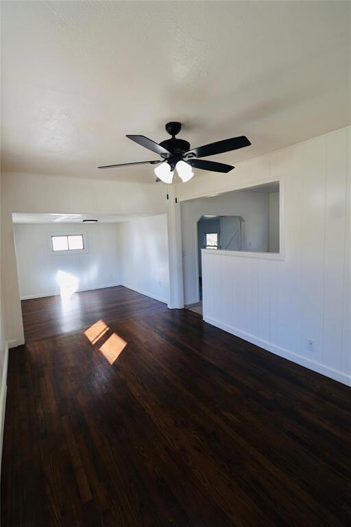 Empty room with dark wood finished floors, a ceiling fan, and wood walls