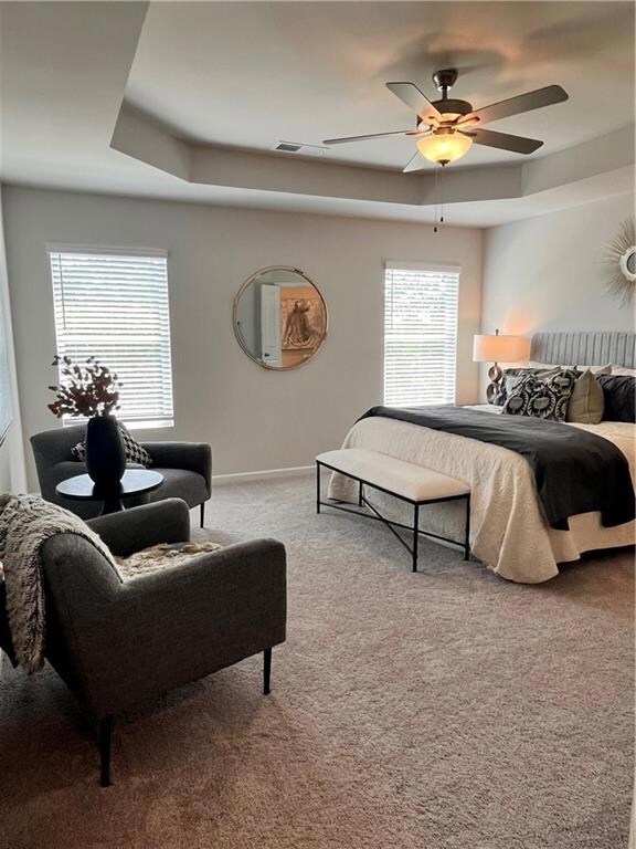 Carpeted bedroom with a raised ceiling, a ceiling fan, and baseboards
