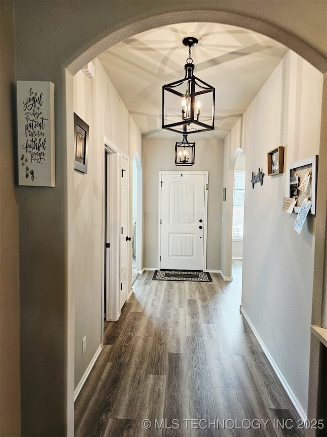 Doorway featuring a chandelier, dark wood-style flooring, arched walkways, and baseboards