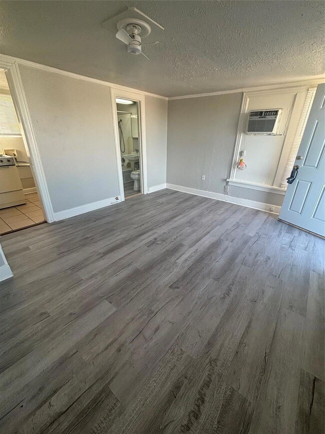 Unfurnished bedroom with ensuite bath, wood-type flooring, a textured ceiling, ceiling fan, and a wall mounted air conditioner