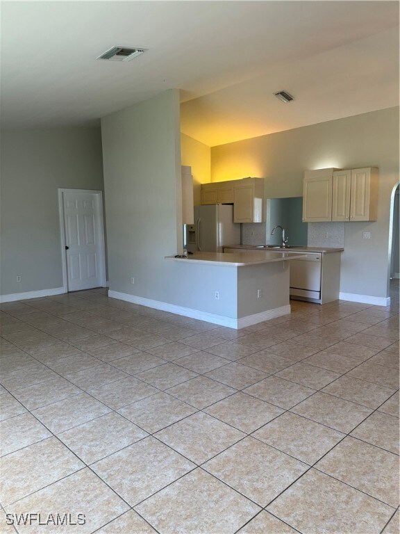 Kitchen with white fridge, vaulted ceiling, light tile patterned flooring, and dishwashing machine
